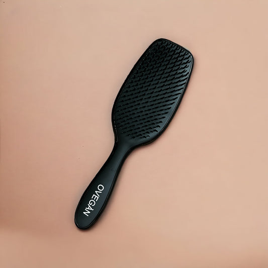 A black hair styling brush with a curved shape, laying on a beige background.